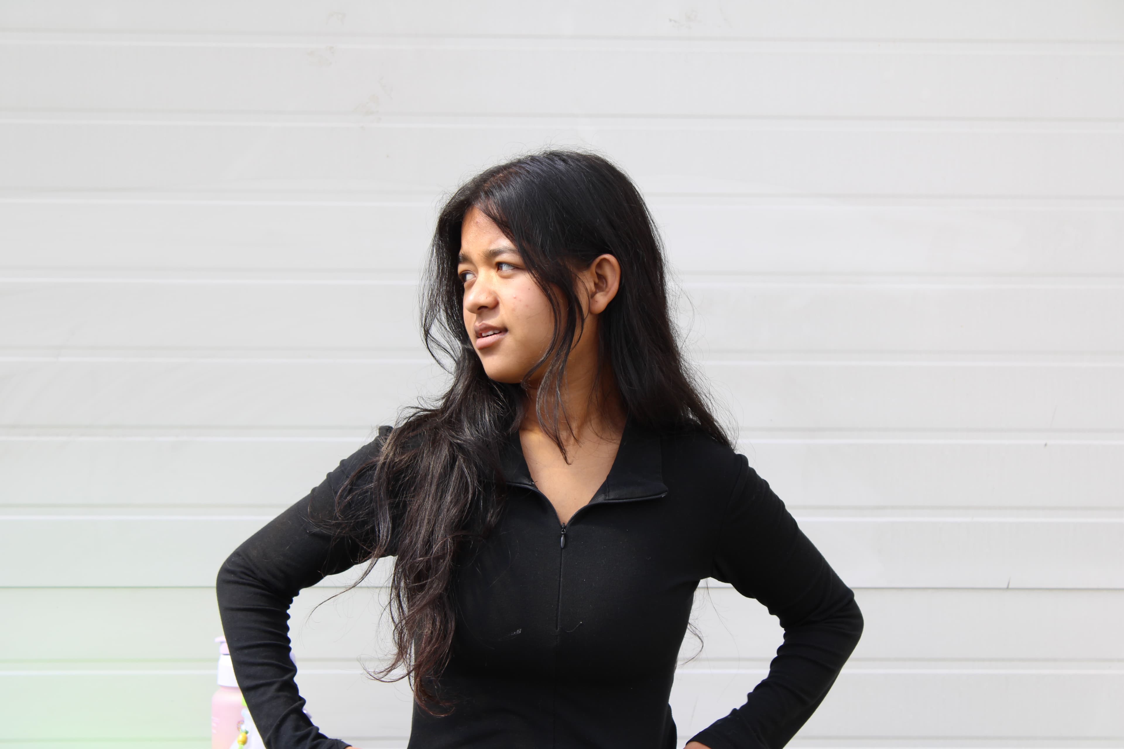 https://media.devpulse.info/A Girl in black outfit is standing in front of white background, looking away from the camera with her hands on her waist.