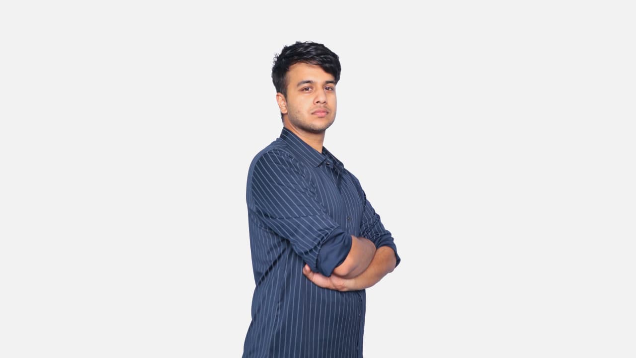 A professional headshot of a young man with dark hair, wearing a dark blue pinstriped collared shirt, with his arms crossed and a neutral expression, looking directly at the viewer against a plain white background.